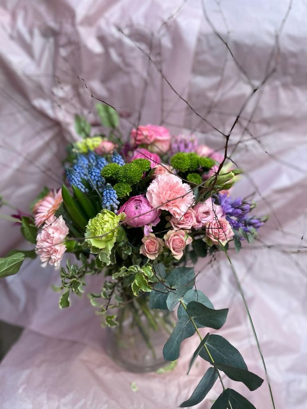 Blumengesteck aus verschieden farbigen Blumen in einer Glasvase vor hellem Hintergrund