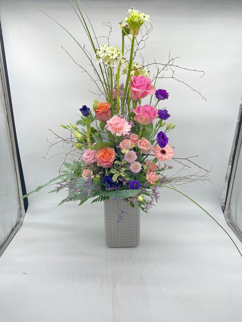 Blumenstrauß aus verschieden farbigen Blumen in einer soliden Vase vor hellem Hintergrund